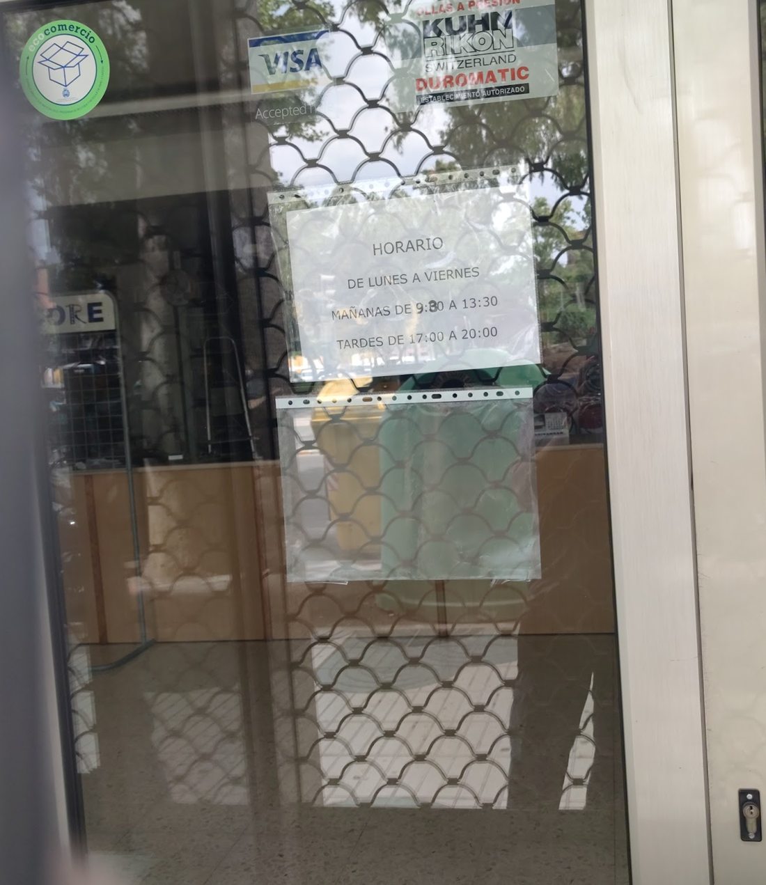 Puerta de la tienda con el cartel del horario y el distintivo de establecimiento autorizado Kuhn Rikon Duromatic